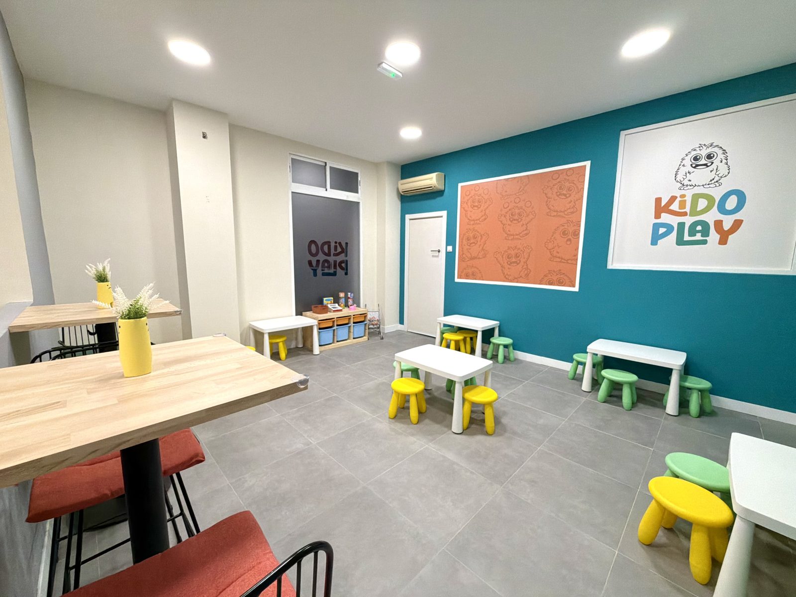 KIDO TALLERES: mesas y taburetes infantiles junto al mural del logotipo de KIDO PLAY